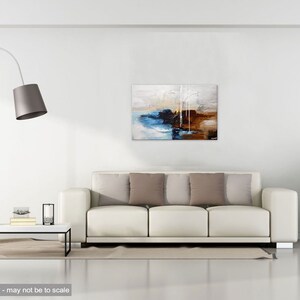 May include: Abstract painting with brown, blue, white, and gray colors. The painting is hanging on a white wall above a white couch with brown pillows.