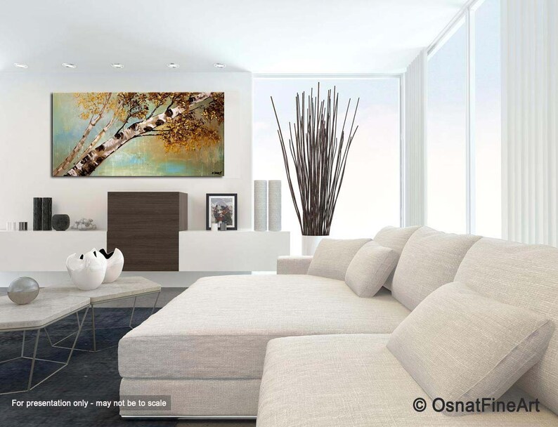 May include: A painting of a birch tree with a white trunk and brown branches against a background of green and brown leaves. The painting is hanging on a white wall in a living room setting with a white couch and pillows.