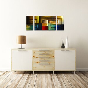 May include: A three-piece abstract art print set featuring geometric shapes in shades of brown, yellow, blue, green, and red. The prints are displayed on a white wall above a wooden dresser with white drawers.