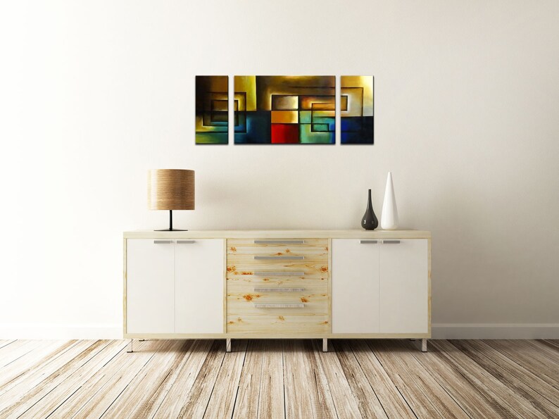 May include: A three-piece abstract art print set featuring geometric shapes in shades of brown, yellow, blue, green, and red. The prints are displayed on a white wall above a wooden dresser with white drawers.