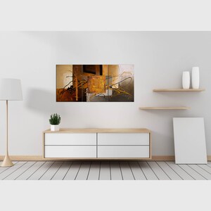May include: Abstract art print with a multi-panel design featuring brown, gold, and black colors. The print is displayed on a white wall above a white dresser with a plant on top.