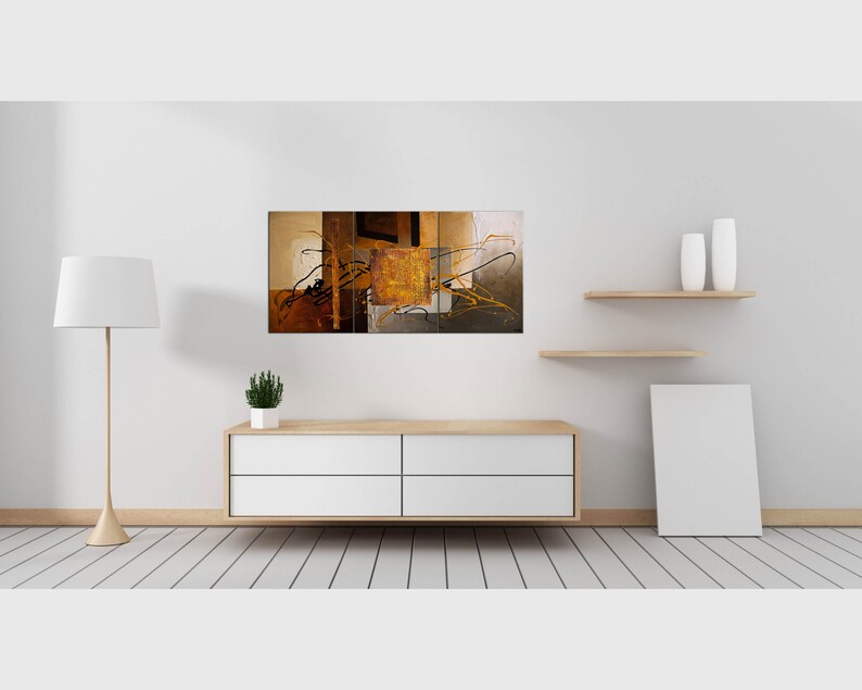 May include: Abstract art print with a multi-panel design featuring brown, gold, and black colors. The print is displayed on a white wall above a white dresser with a plant on top.