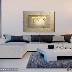 May include: Abstract painting of three stylized trees with white and gold accents on a textured canvas. The painting is framed in a gold frame and is displayed on a wall in a living room setting.