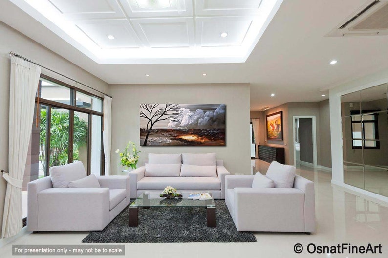 May include: A living room interior with a white couch, two white armchairs, and a glass coffee table. A large abstract painting of a tree and clouds hangs on the wall above the couch. The painting is done in shades of gray, white, and brown.