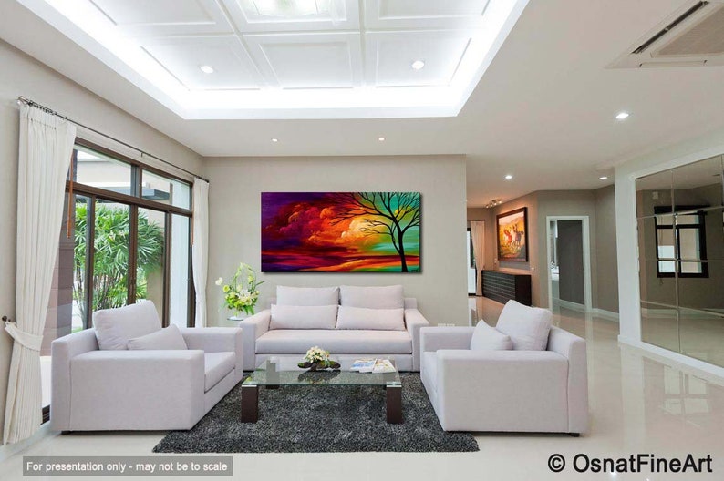 May include: Abstract painting of a colorful landscape with a tree in the foreground. The painting is displayed on a wall in a living room with white furniture.