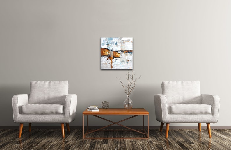 May include: Abstract painting with white, blue, and brown paint strokes. The painting is framed and hanging on a white wall above a brown coffee table.