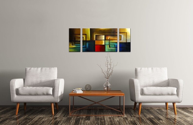 May include: A set of four abstract paintings with geometric shapes in shades of blue, green, yellow, red, and brown. The paintings are arranged in a horizontal row on a white wall above a wooden coffee table.