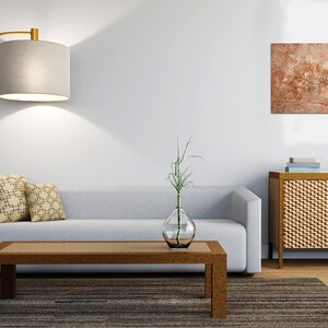 May include: A modern living room with a gray sofa, a brown coffee table, and a gold floor lamp with a beige lampshade. Two decorative pillows with a geometric pattern rest on the sofa. A piece of abstract art hangs on the wall.