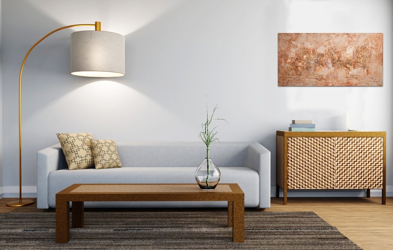 May include: A modern living room with a gray sofa, a brown coffee table, and a gold floor lamp with a beige lampshade. Two decorative pillows with a geometric pattern rest on the sofa. A piece of abstract art hangs on the wall.