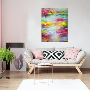 May include: Abstract painting with vibrant colors of pink, yellow, green, and blue. The painting is hanging on a white wall above a light gray couch with pillows.