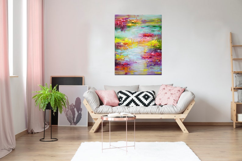 May include: Abstract painting with vibrant colors of pink, yellow, green, and blue. The painting is hanging on a white wall above a light gray couch with pillows.