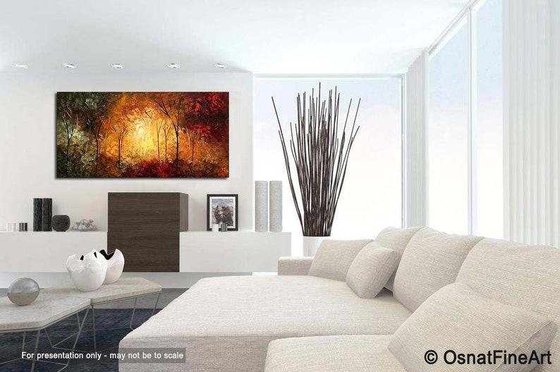 May include: A painting of a forest scene with trees in shades of green, brown, and red. The trees are silhouetted against a bright orange and yellow sky. The painting is hanging on a white wall in a modern living room.
