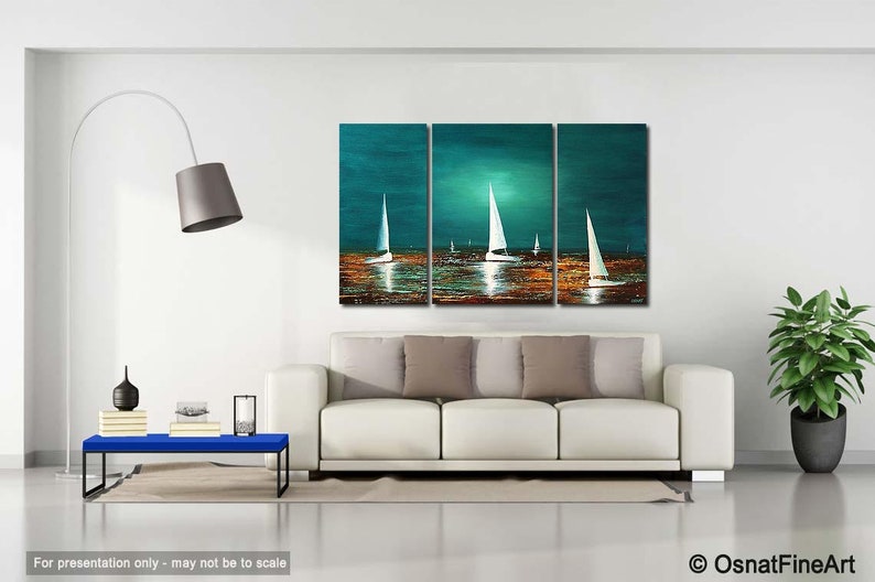May include: A three-piece abstract painting of sailboats on a teal blue ocean with a golden sunset. The painting is displayed on a white wall above a white couch with brown throw pillows.