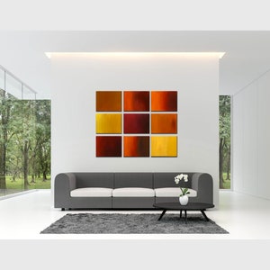 May include: A modern living room with a gray sofa and a set of eight abstract paintings in shades of orange, red, and yellow hanging on the wall.