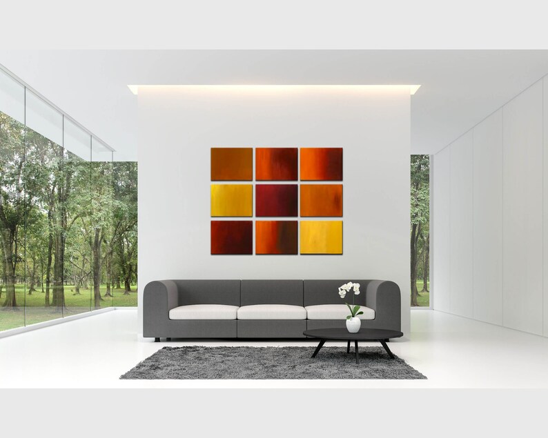 May include: A modern living room with a gray sofa and a set of eight abstract paintings in shades of orange, red, and yellow hanging on the wall.