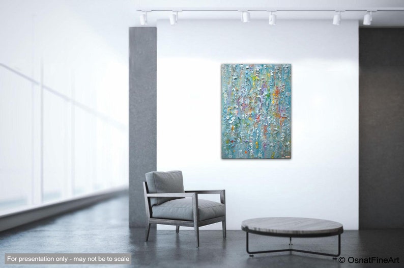 May include: Abstract painting with a textured surface in shades of blue, white, and yellow. The painting is hanging on a white wall in a modern living room setting.