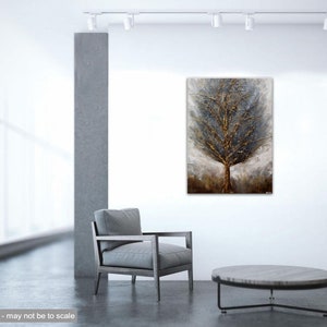 May include: A textured abstract painting of a tree with gold and silver accents. The tree is set against a background of muted gray and brown tones. The painting is displayed in a modern interior setting with a gray armchair and a round coffee table.
