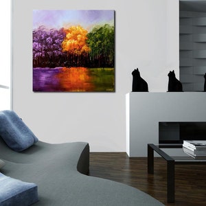 May include: Abstract painting of a forest scene with purple, yellow, and green trees reflected in a still body of water. The painting is framed and hanging on a white wall.