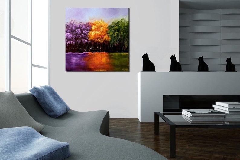 May include: Abstract painting of a forest scene with purple, yellow, and green trees reflected in a still body of water. The painting is framed and hanging on a white wall.