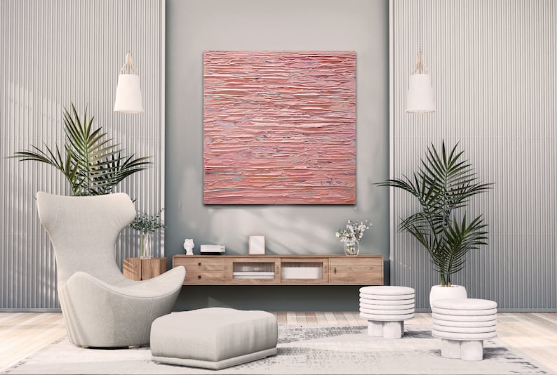 May include: A modern living room interior with a pink abstract painting hanging on the wall above a wooden media console. The room features a white armchair, a white ottoman, two white plant stands with potted plants, and a white rug.