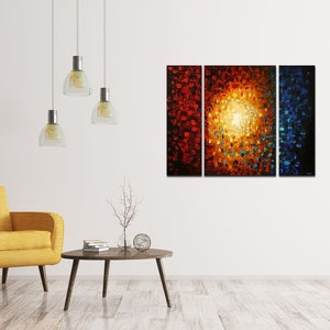 May include: A three-piece abstract painting with a bright yellow center surrounded by red, orange, and blue hues. The painting is displayed on a white wall in a living room setting with a yellow armchair and a coffee table.