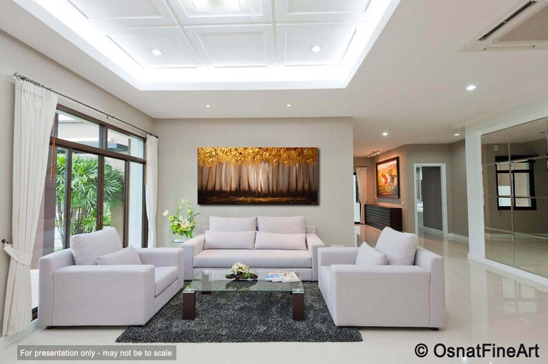 May include: A living room interior design featuring a large abstract painting of a forest scene in gold and brown tones. The painting is hung on a wall above a white sofa and two armchairs. The room has a white ceiling with recessed lighting and a large window with white curtains.