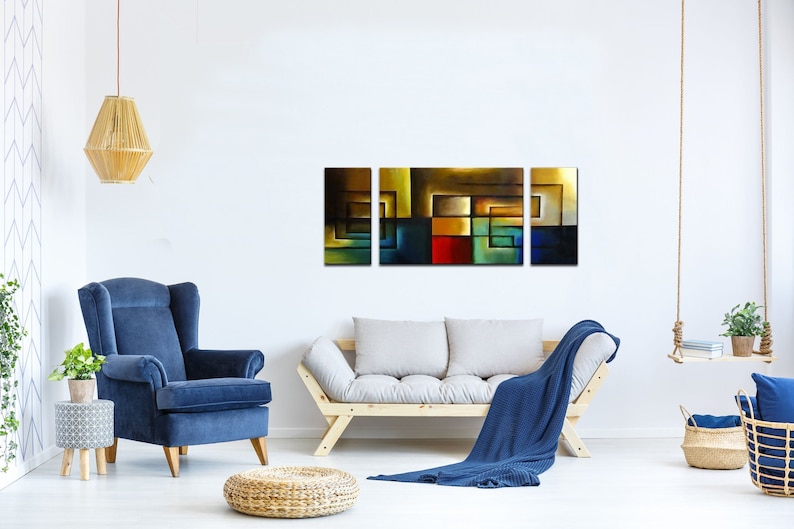 May include: A three-piece abstract art print set featuring geometric shapes in shades of blue, green, red, yellow, and brown. The artwork is displayed on a white wall above a couch and a blue armchair.