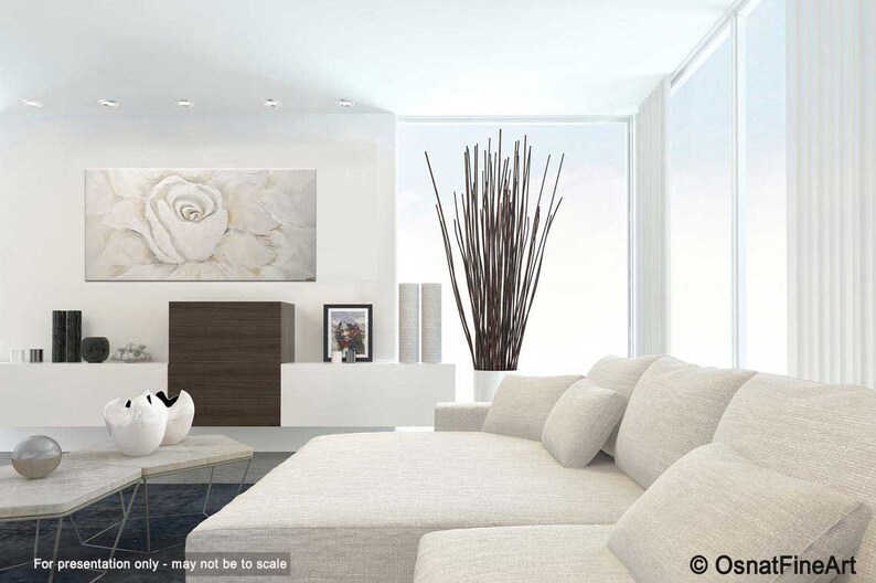 May include: A white, abstract painting of a single rose with a light brown background. The painting is hanging on a white wall in a modern living room with a white sectional sofa and a vase of brown branches.
