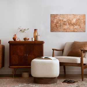 May include: An interior design scene featuring a brown leather sofa, a wooden cabinet, and a cream-colored armchair. A large abstract painting hangs on the wall. A white ottoman and a black rotary phone add to the room's decor.
