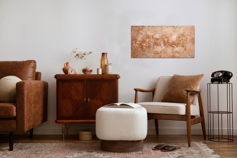 May include: An interior design scene featuring a brown leather sofa, a wooden cabinet, and a cream-colored armchair. A large abstract painting hangs on the wall. A white ottoman and a black rotary phone add to the room's decor.