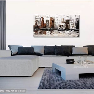May include: A white, gray, and brown abstract painting of a cityscape with a reflection of the buildings in the water below. The painting is hanging on a white wall above a gray sectional sofa with black pillows. A white coffee table sits in front of the sofa.