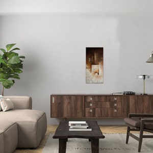 May include: A living room interior design with a brown couch, a wooden cabinet, a brown armchair, a green plant, and a painting with abstract geometric shapes in shades of brown, beige, and white.