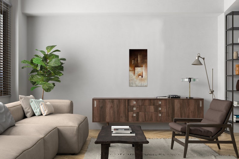 May include: A living room interior design with a brown couch, a wooden cabinet, a brown armchair, a green plant, and a painting with abstract geometric shapes in shades of brown, beige, and white.