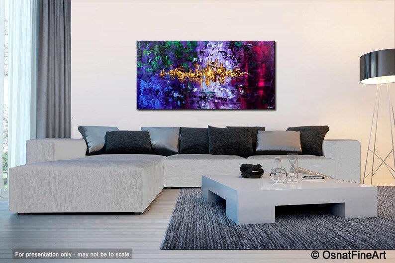 May include: Abstract painting with a mix of purple, green, and gold colors. The painting is displayed on a white wall above a white couch with black pillows.