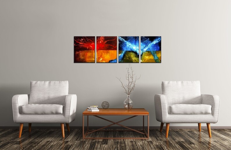 May include: Four abstract paintings in a living room setting. The paintings are in a modern style and feature splashes of red, orange, blue, and yellow paint. The paintings are hung on a white wall above a wooden coffee table. Two white armchairs are placed on either side of the coffee table.