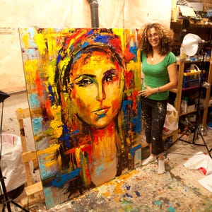 May include: A large, colorful abstract portrait painting of a woman with a yellow and orange face, blue and yellow head covering, and red and blue accents. The painting is on an easel.