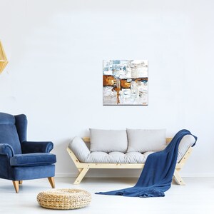 May include: A living room interior with a blue armchair, a wooden sofa with a blue throw blanket, and a modern abstract painting on the wall. The painting features a mix of white, brown, and blue colors.