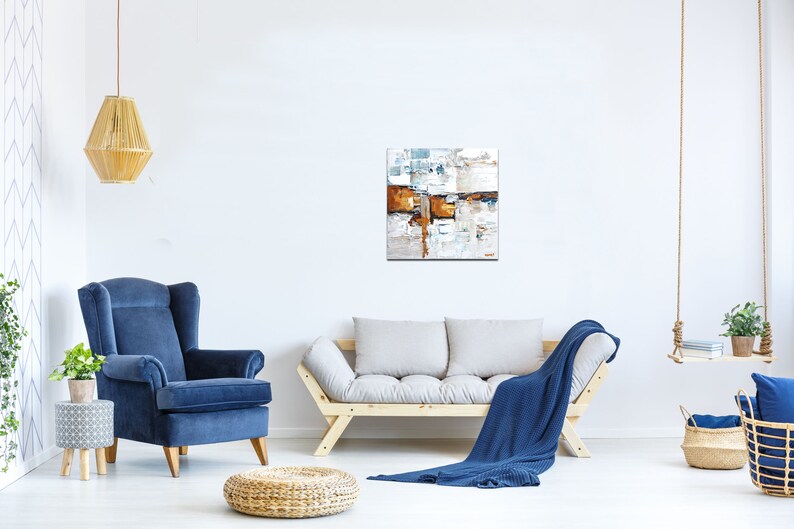 May include: A living room interior with a blue armchair, a wooden sofa with a blue throw blanket, and a modern abstract painting on the wall. The painting features a mix of white, brown, and blue colors.