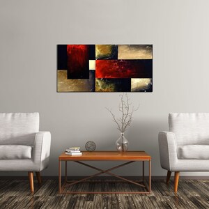 May include: Abstract painting with geometric shapes in shades of black, red, gold, and brown. The painting is hanging on a white wall above a wooden coffee table with two white armchairs.
