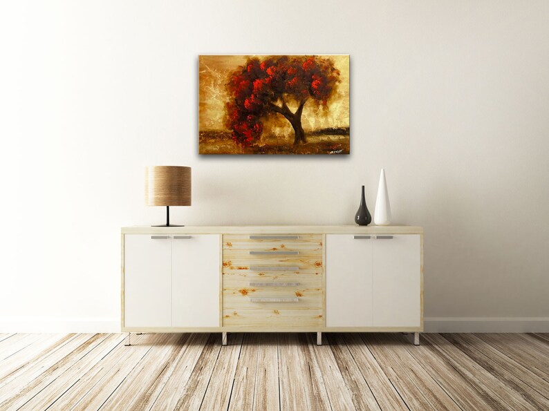 May include: A painting of a tree with red leaves against a gold background. The tree is in the center of the painting and is surrounded by a field of grass. The sky is a light blue color.