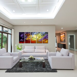 May include: A living room interior with a white sofa and two armchairs. A large abstract painting of a sunset with clouds and a tree hangs on the wall. The painting is in five panels.