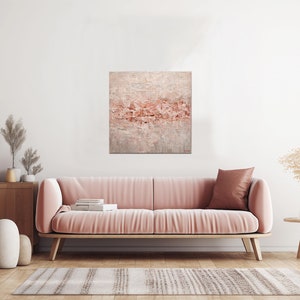 May include: A pink velvet sofa with a throw pillow in a living room setting. A painting with a pink and white abstract design hangs on the wall above the sofa.