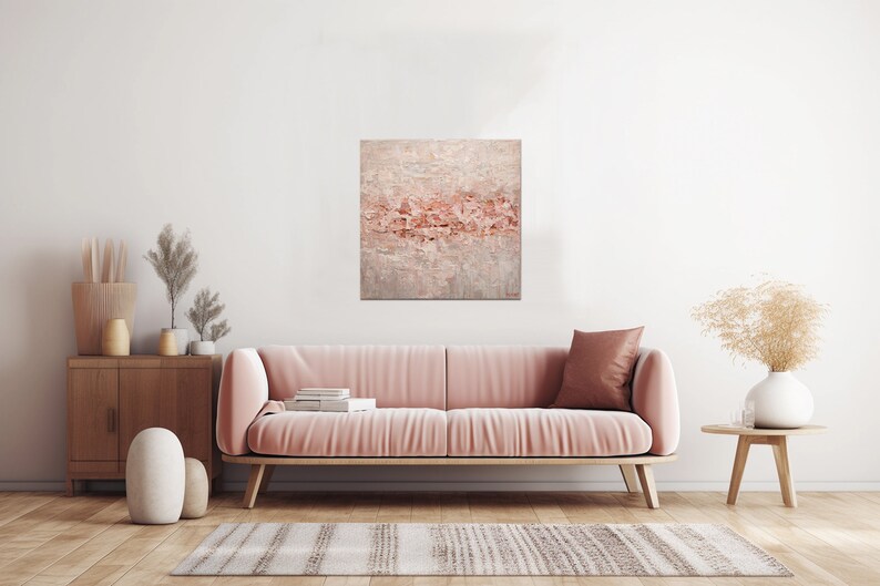 May include: A pink velvet sofa with a throw pillow in a living room setting. A painting with a pink and white abstract design hangs on the wall above the sofa.