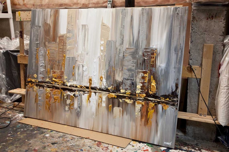 May include: Abstract painting of a cityscape in shades of gray, white, and gold. The painting has a textured surface and appears to be done with a palette knife.