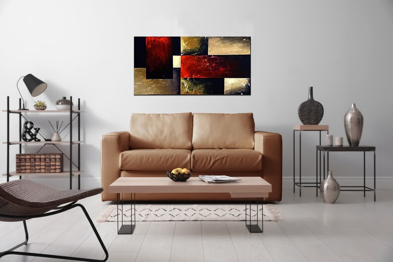 May include: Abstract painting with geometric shapes in shades of red, gold, and black. The painting is displayed on a wall in a living room setting with a brown leather sofa, a coffee table, and decorative items.