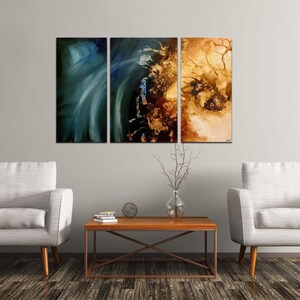May include: Three abstract paintings in a living room setting. The paintings are in shades of blue, green, brown, and gold. The paintings are hung on a light gray wall above a brown coffee table and two white armchairs.
