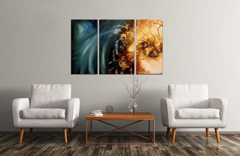 May include: Three abstract paintings in a living room setting. The paintings are in shades of blue, green, brown, and gold. The paintings are hung on a light gray wall above a brown coffee table and two white armchairs.