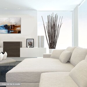 May include: Abstract painting with blue, brown, and white colors. The painting is hanging on a white wall in a modern living room with a white couch and a vase of brown branches.