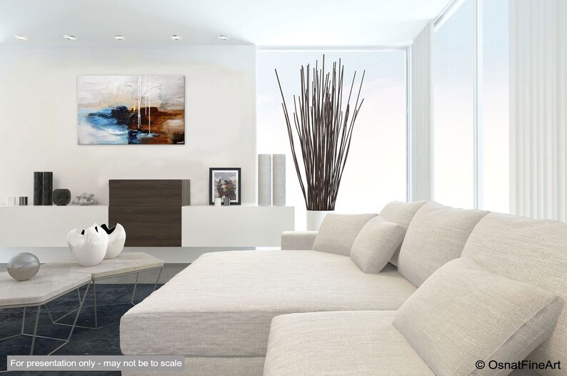 May include: Abstract painting with blue, brown, and white colors. The painting is hanging on a white wall in a modern living room with a white couch and a vase of brown branches.