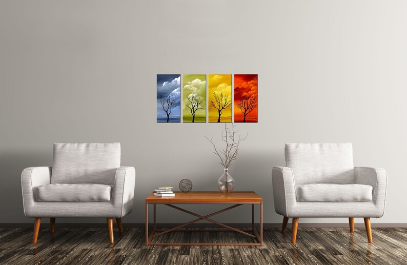 May include: Four abstract paintings of a bare tree against a colorful sky. The paintings are in shades of blue, yellow, orange, and red. The paintings are hung on a white wall above a wooden coffee table and two white armchairs.